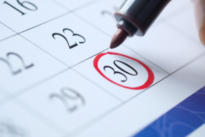 Close-up of a calendar with the 30th circled in red and a marker resting above
